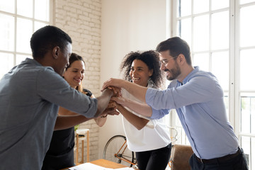 Four millennial different ethnicity teammates stacked palms together feels unity and support. Celebrating profitable deal, common success, leadership in market, participating in team building concept