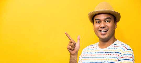 Young happy&funny asian man pointing finger on blank space for text on yellow background.