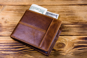 Brown leather wallet and one hundred dollar banknotes on the wooden background