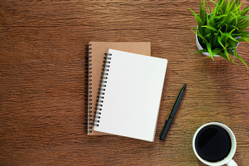 Top view from above of Blank open notebook and coffee on wood table background. Workplace for the creative work of designer at home. Flat lay, Business-finance or education concept with copy space.