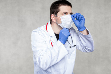 a doctor in protective clothing shows how to put on a protective mask