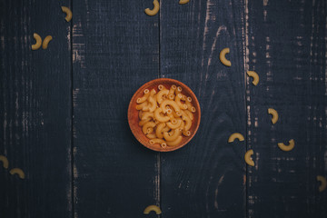 Brown wooden bowl or pot with pasta or raw macaroni on black wooden background, copy space. Carbohydrates diet, healthy eating habits and vegetarian food concept.