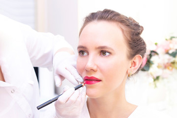 Young woman having permanent makeup on her lips at the beauticians salon. Permanent Makeup...