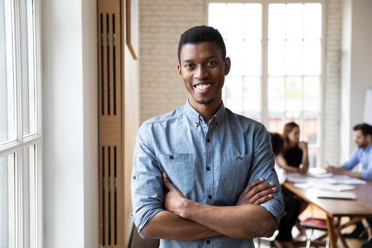 Millennial african ethnicity staff member with arms crossed feels confident posing in modern office boardroom looking at camera. Hired happy employee, executive manager portrait, company boss concept