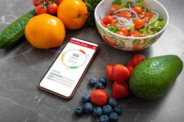 Smartphone with healthy meal planning app on a kitchen counter surrounded by vegetables and fruits