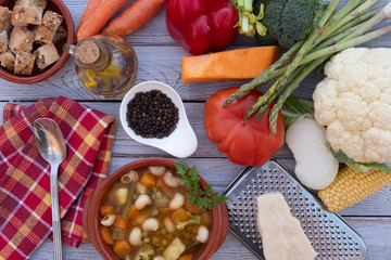 Healthy eating with a fresh, ready-to-eat homemade vegetable soup. Raw vegetables on the wooden table, black pepper, olive oil, croutons and parmesan
