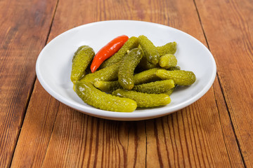 Pickled gherkins on white saucer on rustic table close-up