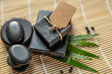 bar block of black carbon charcoal coal soap on a bamboo background with lava stones spa concept