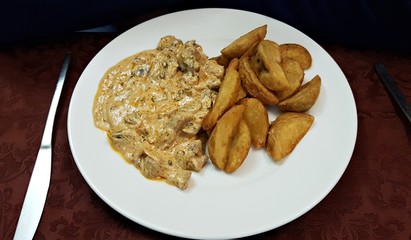 Sliced cooked meat with mushroom sauce and potatoes on a white plate