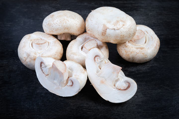 Whole and halves of uncooked button mushrooms on black surface