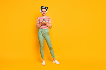 Fototapeta premium Full length photo of pretty lady use telephone turn on favorite melody modern technology earphones wear red white shirt green pants footwear isolated bright yellow color background