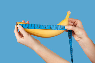 Measuring the size of a banana as a symbol of the male penis isolated on blue background. Big dick...