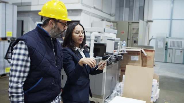 Side view of young boss giving instructions to mature engineer. Two factory workers walking at plant with tablet. Print manufacturing concept