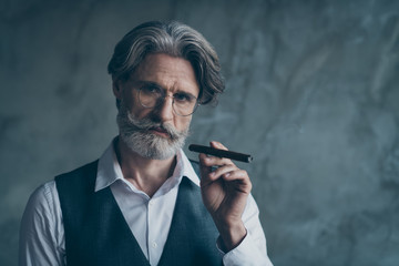 Portrait of harsh masculine brutal stunning old man hold cigar enjoy his rest in big successful company wear shirt isolated over concrete wall grey color background