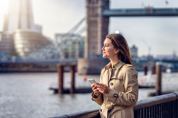 Portrait einer attraktiven Geschäftsfrau mit Mobiltelefon in der Hand vor der Skyline von London, Großbritannien © moofushi