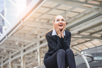 a businesswoman sitting on top of stairway with hands on her cheeks and smiley face feeling overjoy, representing success or happiness in a workplace, in the city with modern architectural structure