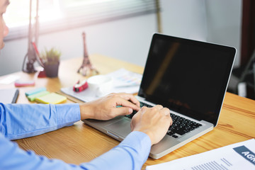asian office worker using and typing on his laptop computer, research and working hard on his business project, working on his wooden table within his office with documentations, calculator and pens