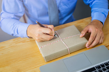 close up of worker using pen writing a house address on brown parcel tied by strings, getting ready...