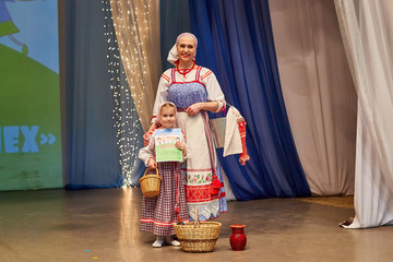 A little girl and an adult woman in Russian national dress posing with a diploma on stage after performing and winning the competition. Mother and daughter standing together