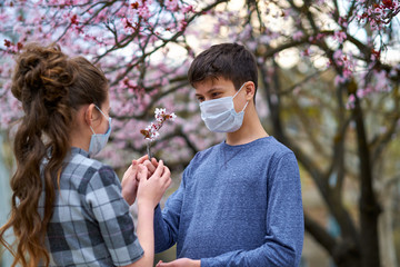 boy and girl with a face mask are in the city outdoor, blooming trees, spring season, flowering time - concept of allergies and health protection from dusty air