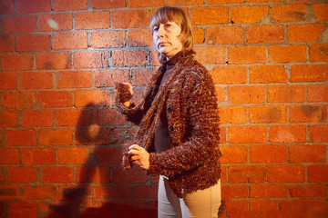 A middle-aged woman poses showing clothes near red brick wall. An inept model in an inept shoot