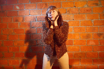 A middle-aged woman poses showing clothes near red brick wall. An inept model in an inept shoot