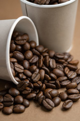 Two gray paper cups with coffee bean. One cup is upset. Close-up.