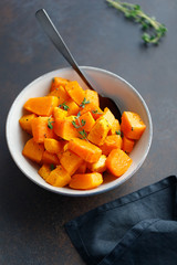 Roasted pumpkin pieces with fresh thyme in a ceramic bowl on a table. Seasonal Autumn recipe.