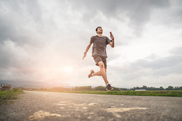 Fototapeta na wymiar asian teen running along the road in sprinting action, exercising or practicing for a marathon race, wearing shirt, short and running shoes with mountain nature and cloudy sunset sky in the background