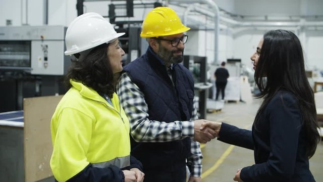 Cheerful project manager shaking hands with technicians. Side view of beautiful Asian woman in suit walking to factory employees and greeting. Cooperation, manufacturing, handshake concept