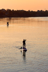 Fototapeta na wymiar Silhouette of woman standing up on paddle board (SUP) on Danube river at sunrise. Backlight