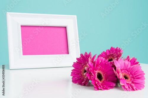 Happy Mother's Day, Women's Day, Valentine's Day or Birthday Pastel Candy Blue Colored Background. Dark pink gerberas on a table with empty picture frame greeting card.