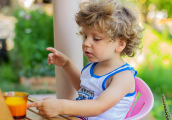 The child has breakfast outdoors. Little boy eats in the yard.