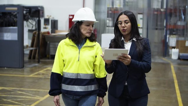Concentrated project manager and technician walking with tablet. Focused professional factory worker listening instructions from boss. Manufacturing, technology concept