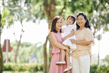 Obraz premium Happy senior Asian woman standing in park with daughter and granddaughter