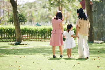 Fototapeta premium Senior woman enjoying spending time with her adult daughter and little granddaughter in park, view from the back