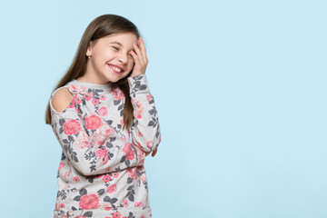 Wow. Studio portrait of an adorable young schoolgirl holding her head in disbelief, isolated on pastel blue background. Human emotions and facial expressions concept.