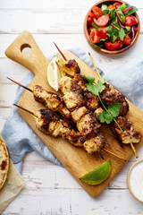 Chicken tikka kebab with red onion, coriander and fresh salad. Traditional indian dish made of chicken marinated in yoghurt and spices. Creative flatlay on white wooden background.