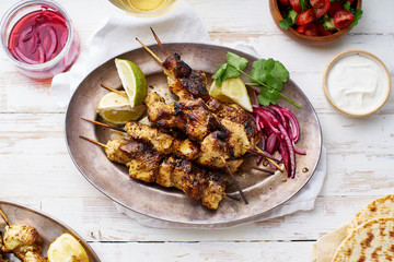 Chicken tikka kebab with red onion, coriander and fresh salad. Traditional indian dish made of chicken marinated in yoghurt and spices. Creative flatlay on white wooden background.