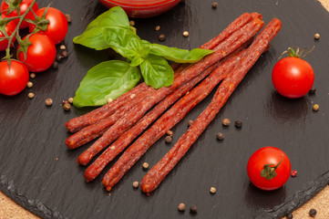 thin long sausage with sauce, cherry tomatoes and basil on a black graphite board