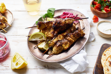 Chicken tikka kebab with red onion, coriander and fresh salad. Traditional indian dish made of chicken marinated in yoghurt and spices. Creative flatlay on white wooden background.