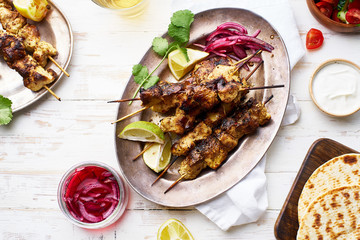 Chicken tikka kebab with red onion, coriander and fresh salad. Traditional indian dish made of chicken marinated in yoghurt and spices. Creative flatlay on white wooden background.