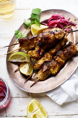 Chicken tikka kebab with red onion, coriander and fresh salad. Traditional indian dish made of chicken marinated in yoghurt and spices. Creative flatlay on white wooden background.