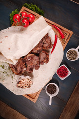 Appetizing fried meat lies on a wooden tray, among the seasonings. Studio photography of food in the cooking industry, dark background