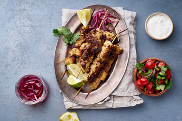 Chicken tikka kebab with marinated onion, fresh salad and yoghurt sauce. Traditional indian cuisine, delicious starter. Creative flatlay