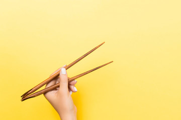 Female hand with chopsticks on yellow background. Traditional asian food with emty space for your design