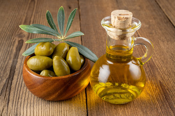 Green olives with olive branch in a small wooden bowl and a small bottle of olive oil on a rustic...