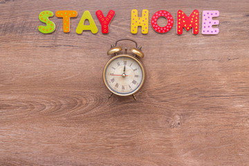 Inscription STAY HOME of wooden letters and alarm clock on wood background with copy space