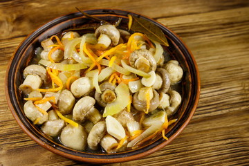 Delicious marinated mushrooms with carrot, onion and spices in ceramic bowl on wooden table