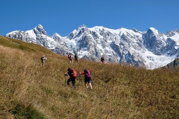 Fototapeta premium Snowy mountains Dzhangi-Tau and Shkhara with Khalde Glacier, with green mountainsides and silhouettes of wandering tourists in foreground. Greater Caucasus, Svaneti, GeorgiaSvaneti